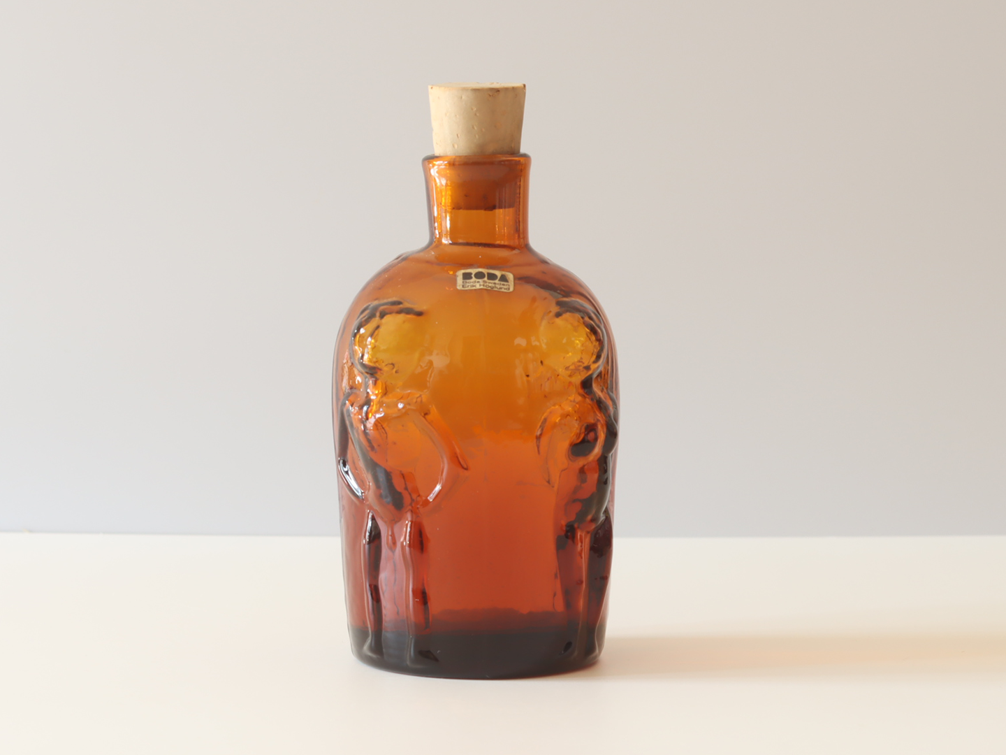 エリック・ホグランがデザインしたBoda（ボダ）社のアンバーカラーのガラスボトル。側面には人物のレリーフが施され、コルク栓と当時のブランドシールが残っているヴィンテージ品です。
